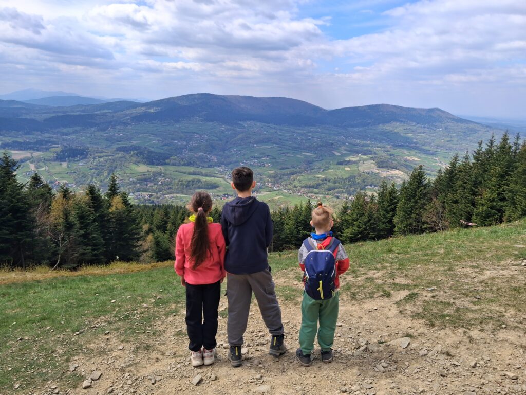 Troje dzieci podziwiają panoramę Beskidów z polany podszczytowej Cietnia