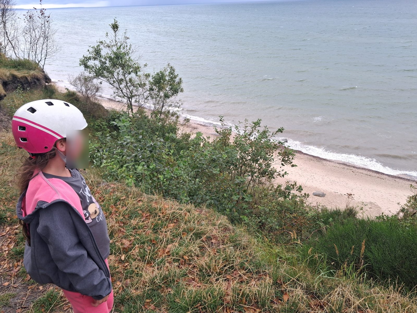 Dziewczynka w kasku rowerowym patrzy z klifu na plażę i Morze Bałtyckie na trasie Rowy – Ustka